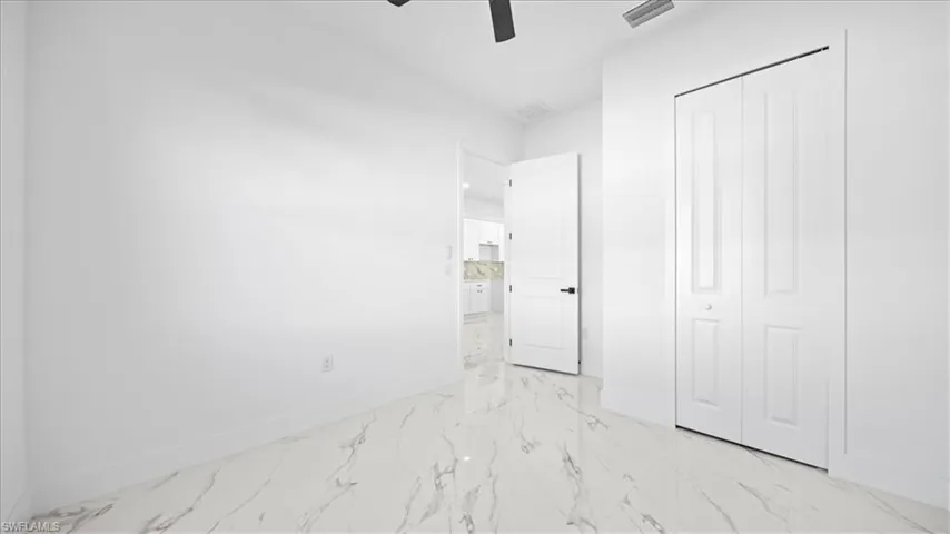 Unfurnished bedroom featuring light marble finish flooring, a ceiling fan, and a closet
