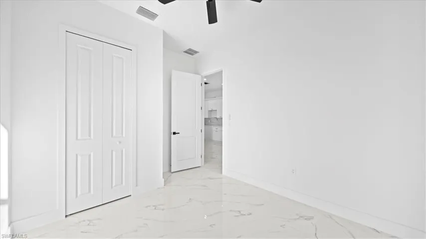 Unfurnished bedroom featuring light marble finish flooring, ceiling fan, and a closet