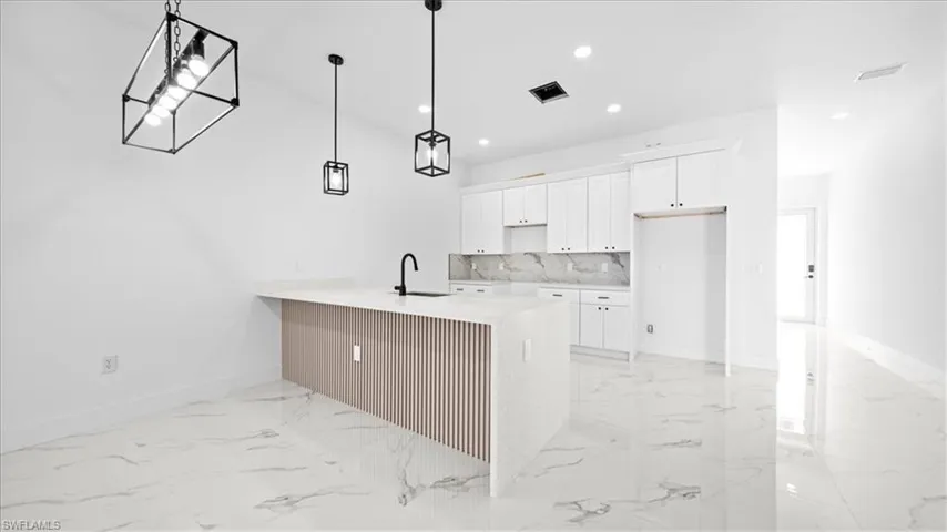 Kitchen featuring a peninsula, white cabinets, a kitchen bar, light stone countertops, and hanging light fixtures