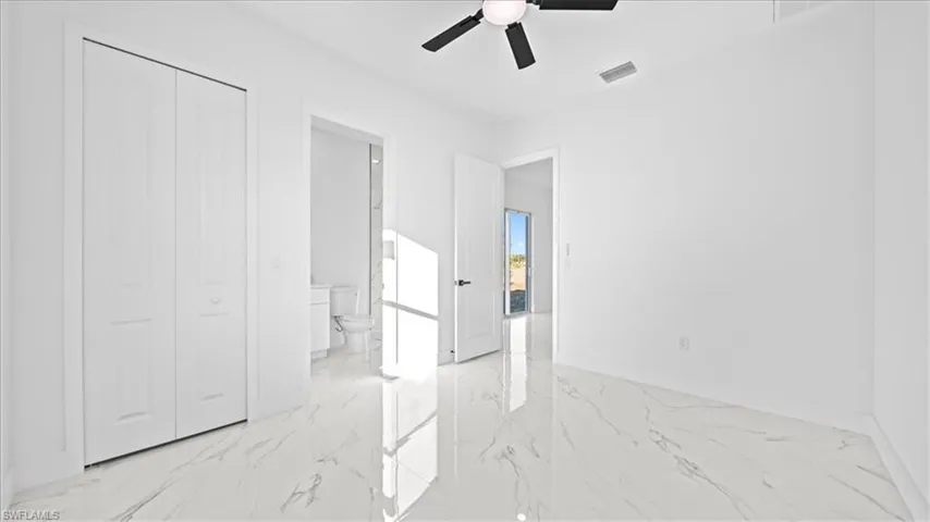 Unfurnished bedroom featuring light marble finish flooring, ceiling fan, ensuite bathroom, and a closet