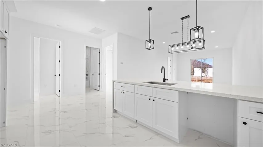 Kitchen with white cabinets, hanging light fixtures, light marble finish floors, recessed lighting, and light stone countertops