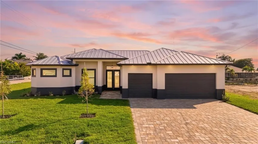 New construction home featuring an attached garage, a standing seam roof, a landscaped front yard, decorative driveway, and stucco siding