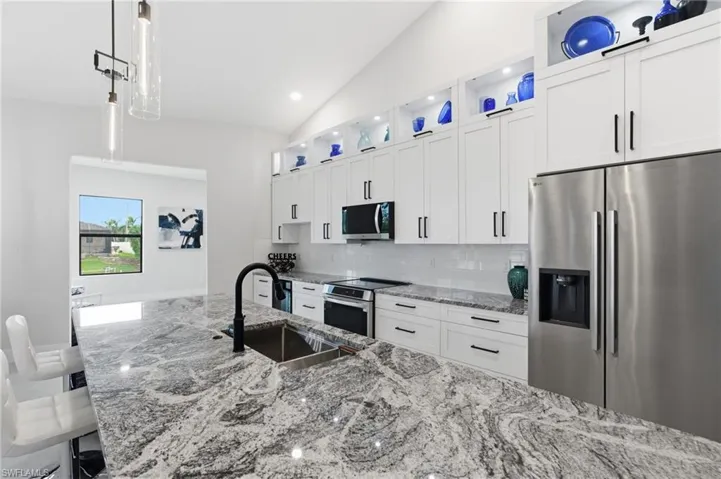 Kitchen with white cabinets, stainless steel appliances, premium countertops, decorative light fixtures, and tasteful backsplash