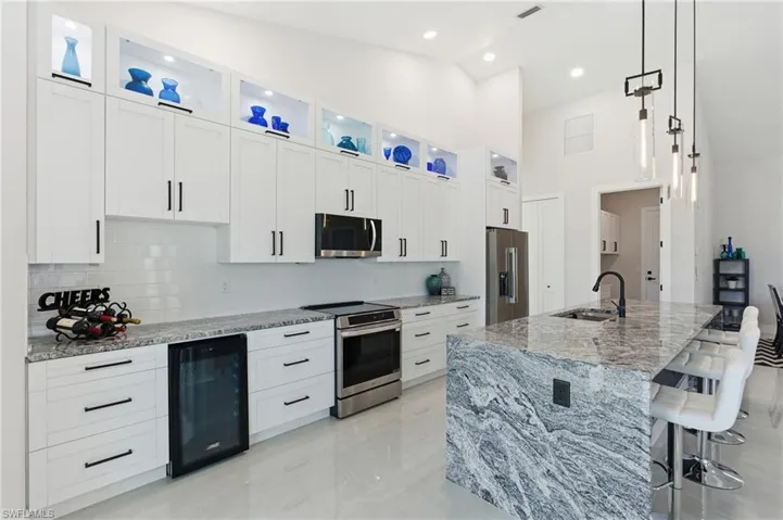 Kitchen with premium counters, stainless steel appliances, white cabinets, beverage cooler, and a breakfast bar