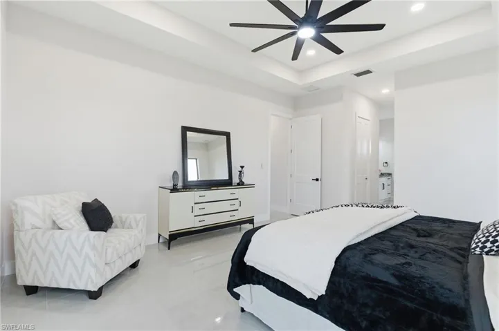Primary bedroom featuring a tray ceiling, ensuite bathroom, ceiling fan, and recessed lighting