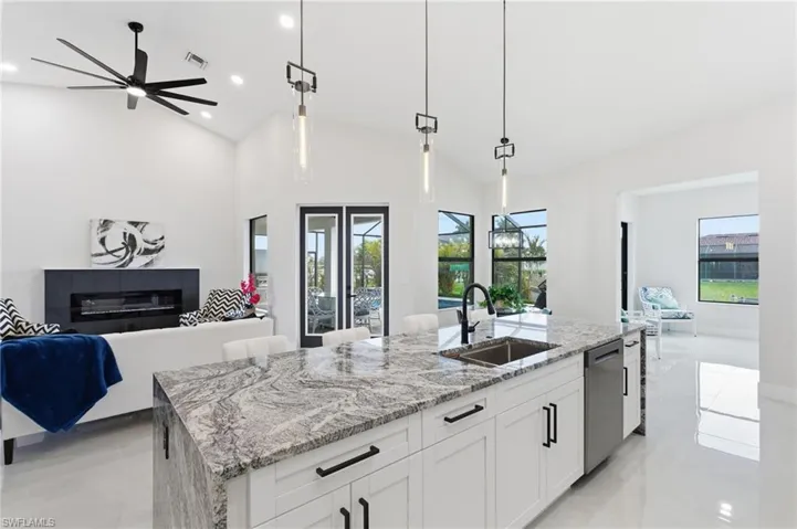 Kitchen featuring open floor plan, premium counters, a ceiling fan, white cabinetry, and a kitchen island with sink