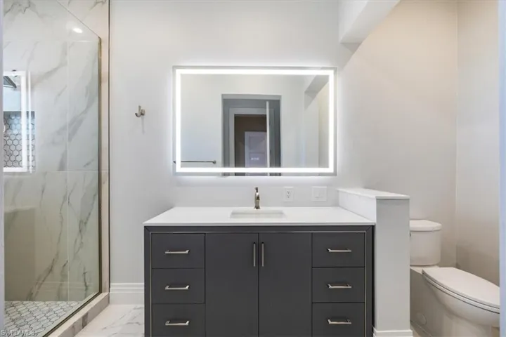 Full bath featuring vanity, a marble finish shower, and light marble finish floors