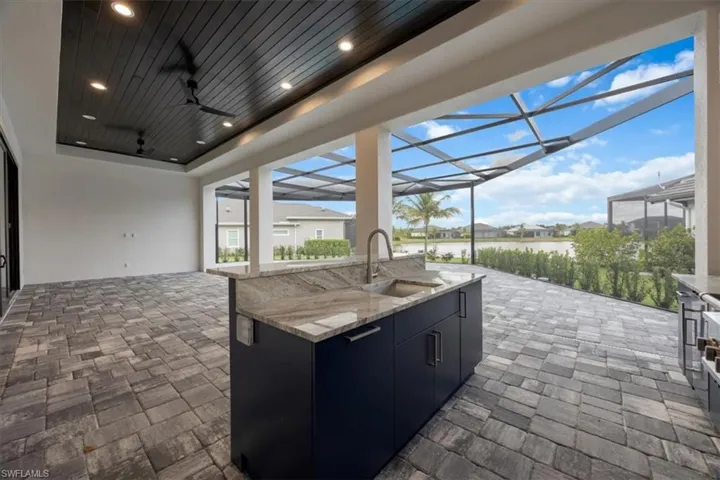 View of patio featuring glass enclosure, a sunroom, ceiling fan, a residential view, and a bar