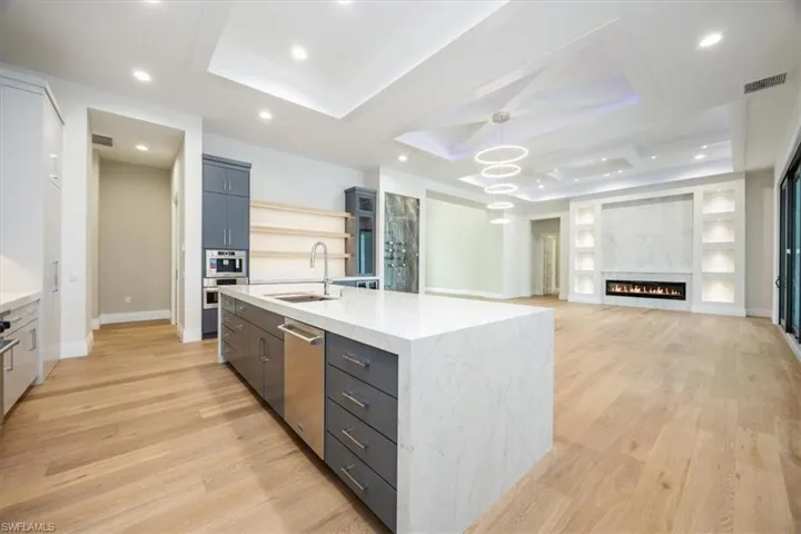 Kitchen featuring light wood finished floors, a kitchen island with sink, open floor plan, open shelves, and decorative light fixtures