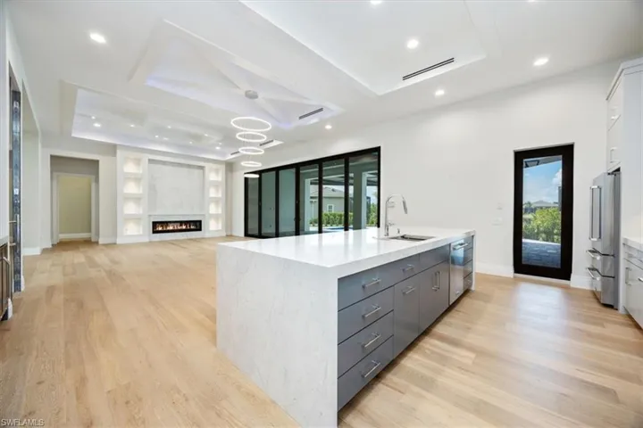 Kitchen featuring open floor plan, a tray ceiling, built in shelves, a center island with sink, and recessed lighting