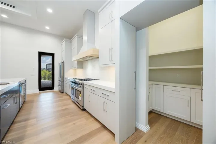 Kitchen featuring white cabinetry, wall chimney range hood, stainless steel appliances, light wood finished floors, and recessed lighting