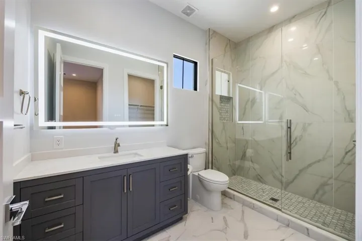 Full bath with a marble finish shower, vanity, light marble finish flooring, and recessed lighting