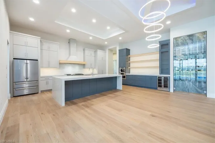 Kitchen featuring open shelves, high end fridge, a tray ceiling, light wood finished floors, and wall chimney exhaust hood