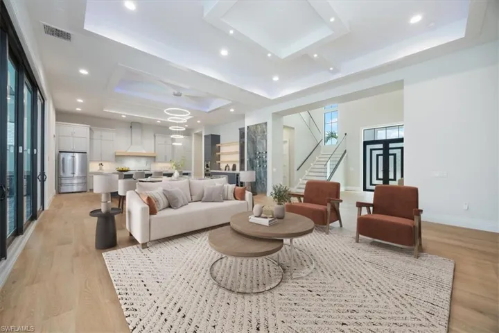 Living room featuring a raised ceiling, light wood-style flooring, stairway, recessed lighting, and a chandelier