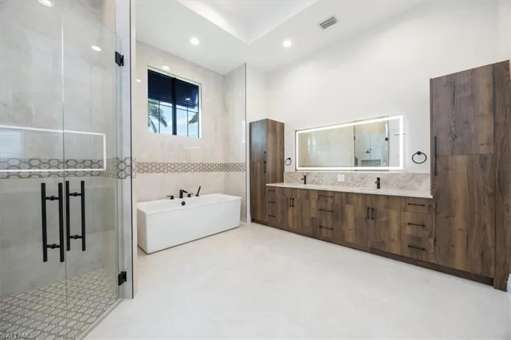 Bathroom with a soaking tub, a shower stall, double vanity, tile walls, and recessed lighting