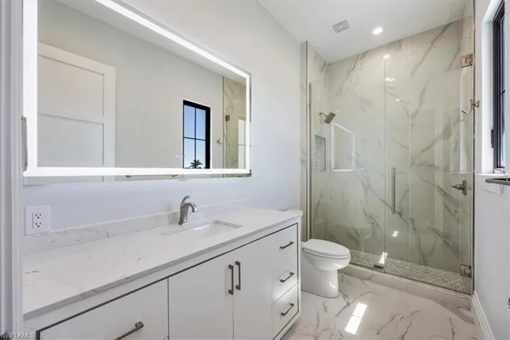 Full bathroom with vanity, a marble finish shower, light marble finish floors, and recessed lighting