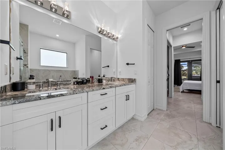 Ensuite bathroom with a closet, double vanity, light marble finish floors, and tiled shower