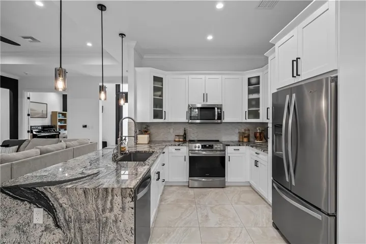 Kitchen featuring dark stone counters, ornamental molding, stainless steel appliances, a peninsula, and white cabinetry