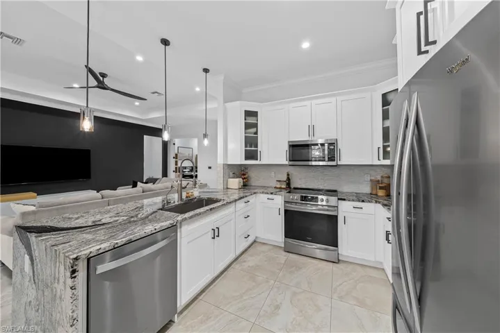 Kitchen with stainless steel appliances, light stone counters, white cabinetry, a peninsula, and crown molding