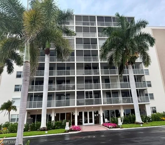 Multi-story residential building featuring screened balconies, white exterior siding, and a ground-floor entrance with glass doors