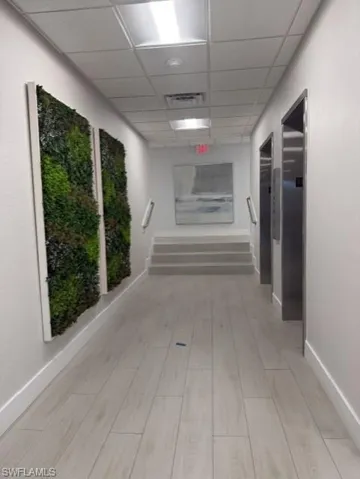 Corridor featuring light wood-finish flooring, white walls, and a dropped ceiling with recessed lighting