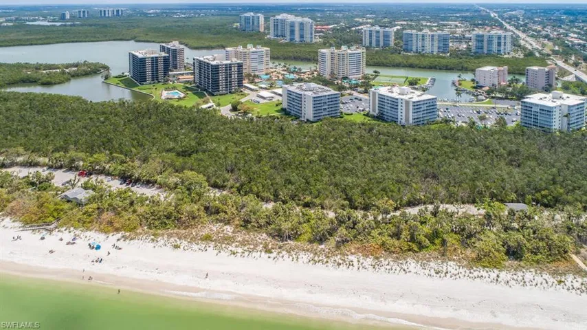 Beachfront property featuring white sand, abundant green foliage, and water access