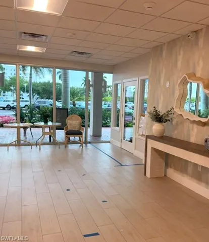 Bright interior space featuring light wood-finish flooring, full-height windows, a decorative wall mirror, and modern ceiling grid lighting