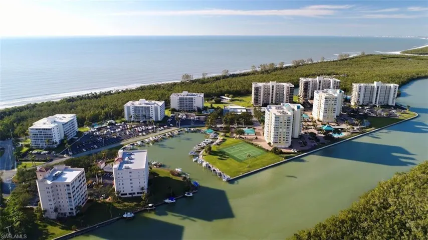 Coastal residential complex featuring multiple high-rise buildings, a marina with boat slips, tennis courts, and a swimming pool area