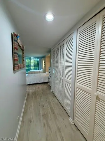 Hallway featuring wood-finish flooring, recessed lighting, and a wall of louvered closet doors