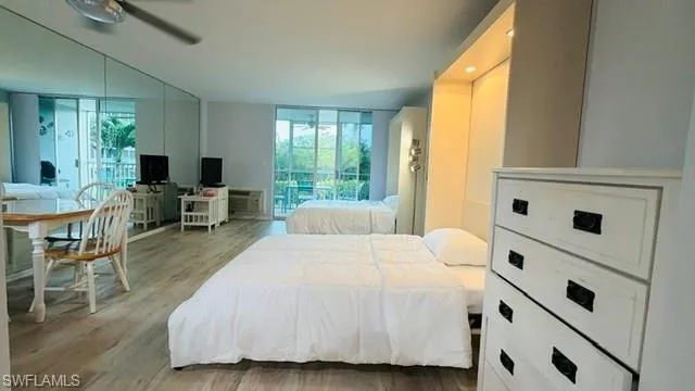 Open-plan living area featuring wood-finish flooring, full wall mirrors, and two sets of sliding glass doors opening to balconies