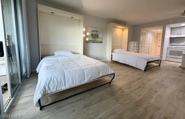 Versatile living area featuring two wall-mounted folding beds, light wood-finish flooring, a full kitchen with white appliances, and sliding glass doors opening to an exterior space