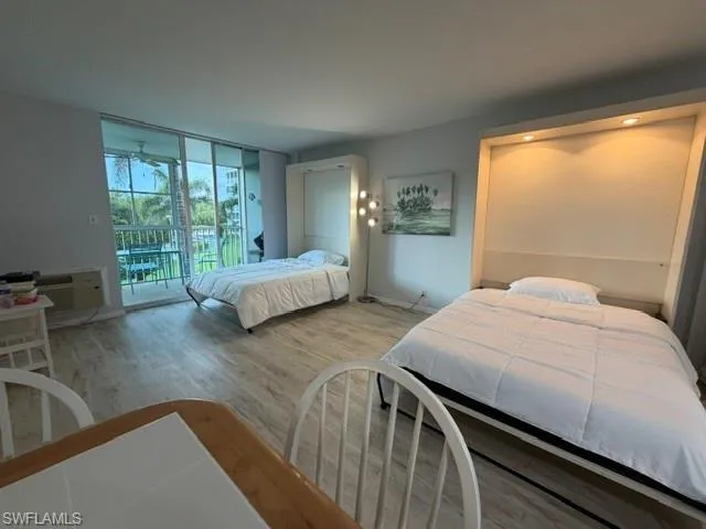 Spacious studio featuring light wood-finish flooring, a wall-mounted murphy bed with recessed lighting, and a second wall-mounted bed