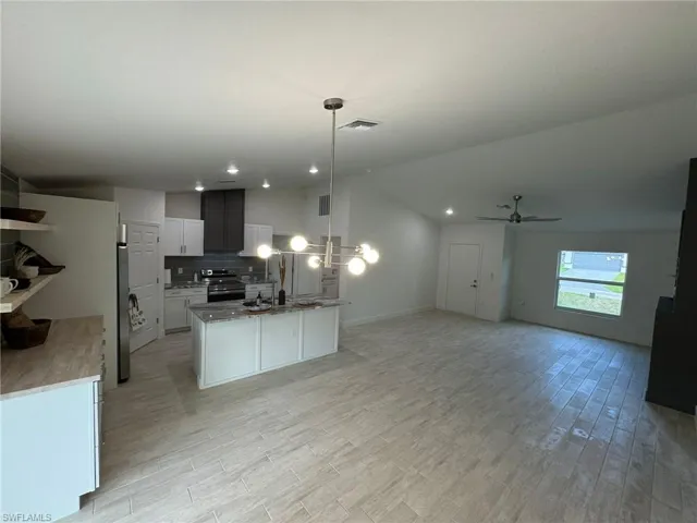 Kitchen featuring open floor plan, stone countertops, light wood-style flooring, a large fireplace, and vaulted ceiling