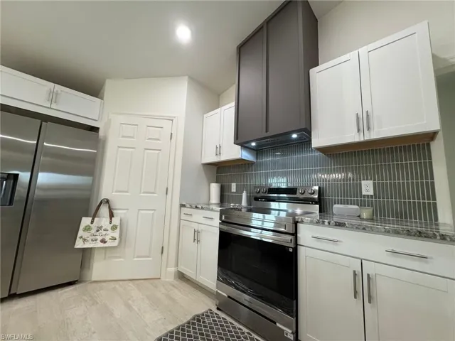Kitchen featuring open shelves, stainless steel refrigerator with ice dispenser, decorative backsplash, white cabinets, and light wood-style flooring