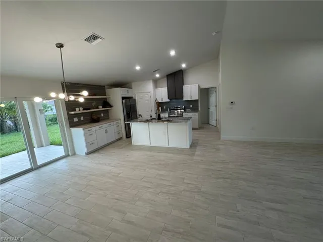 Kitchen with open floor plan, lofted ceiling, appliances with stainless steel finishes, white cabinetry, and ceiling fan