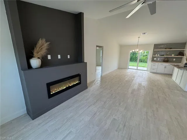 Unfurnished living room featuring a large fireplace, vaulted ceiling, a chandelier, ceiling fan, and light wood-style floors