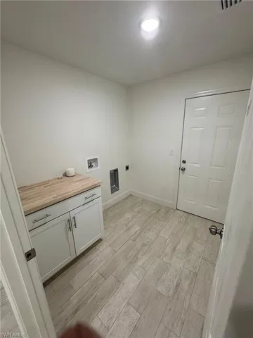 Washroom with hookup for an electric dryer, washer hookup, light wood-style flooring, and cabinet space