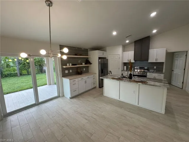 Kitchen with stainless steel appliances, light stone countertops, tasteful backsplash, and white cabinetry