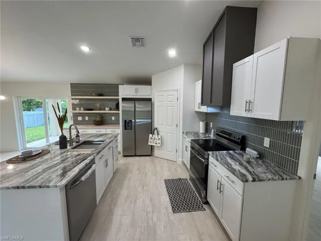 Kitchen featuring vaulted ceiling, open floor plan, tasteful backsplash, refrigerator with ice dispenser, and white cabinetry