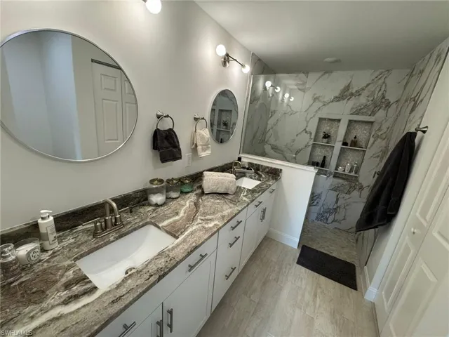 Full bathroom with a marble finish shower, double vanity, and wood finished floors