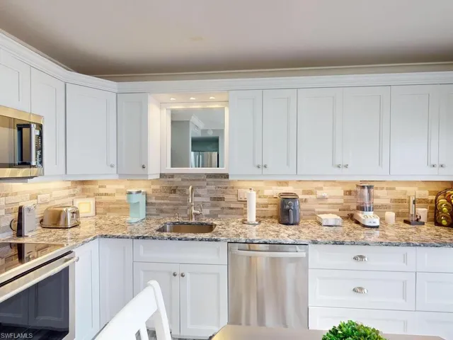 Kitchen with backsplash, sink, white cabinets, and appliances with stainless steel finishes