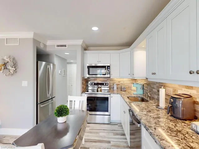 Kitchen with tasteful backsplash, sink, white cabinets, and appliances with stainless steel finishes