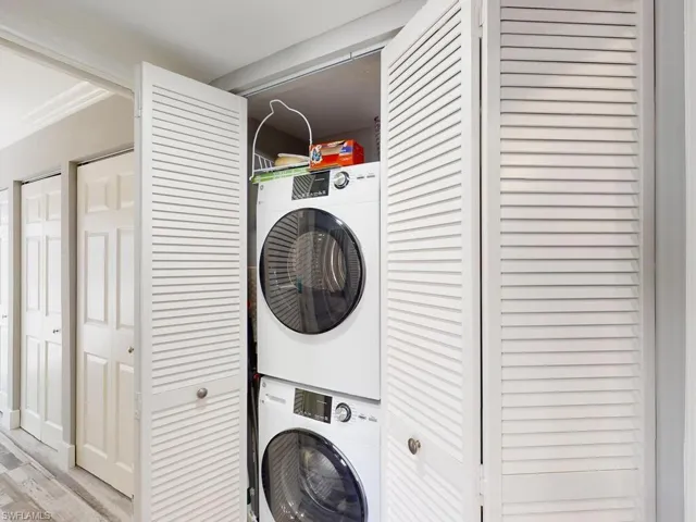 Clothes washing area featuring ornamental molding, light hardwood / wood-style flooring, and stacked washer and clothes dryer