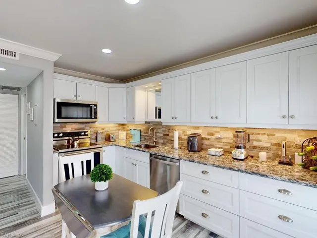 Kitchen with white cabinets, sink, ornamental molding, appliances with stainless steel finishes, and tasteful backsplash