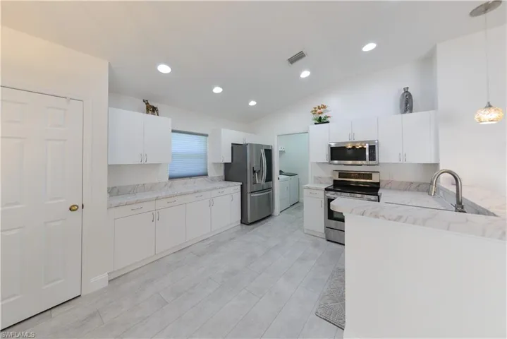 Kitchen featuring white cabinetry, stainless steel appliances, hanging light fixtures, and washing machine and dryer
