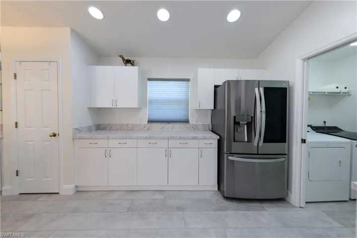 Kitchen with stainless steel fridge with ice dispenser, vaulted ceiling, separate washer and dryer, and white cabinets