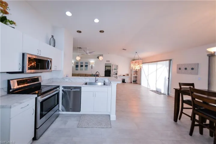 Kitchen featuring white cabinets, appliances with stainless steel finishes, lofted ceiling, and sink