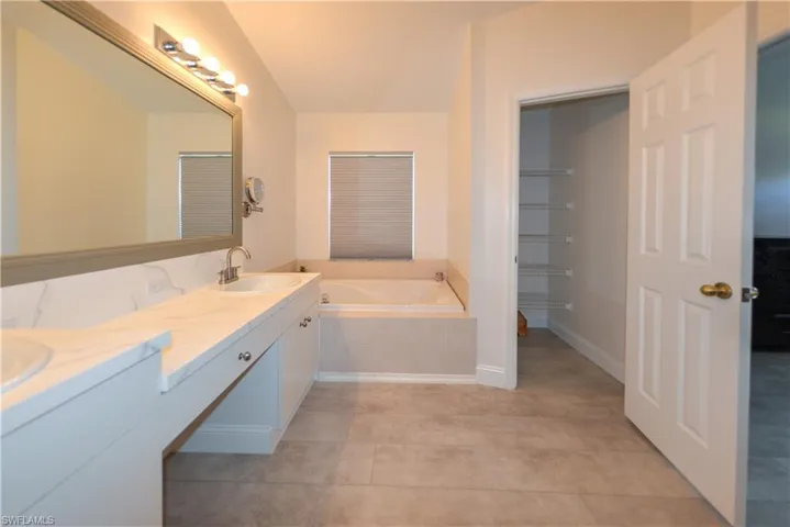 Bathroom with vanity, tile patterned floors, and tiled tub