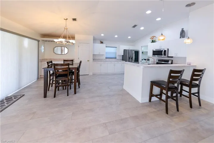 Kitchen with white cabinetry, kitchen peninsula, appliances with stainless steel finishes, decorative light fixtures, and vaulted ceiling