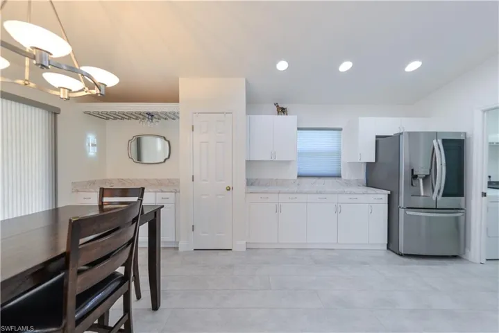 Kitchen with white cabinets, light tile patterned flooring, pendant lighting, and stainless steel fridge with ice dispenser